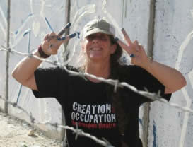 photo of Rabbi Lynn Gottlieb with paint on fingers, standing behind barbed wire wearing t-shirt that says Creation/Occupation